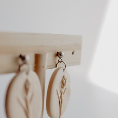 Brincos ovais bege com relevo de flor pendurados em suporte de madeira