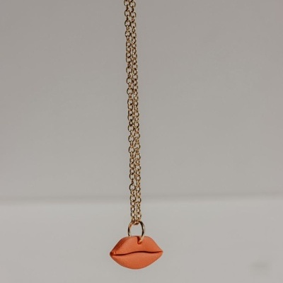 Colar dourado com pendente em forma de lábios alaranjados
