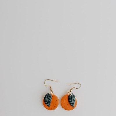 Brincos com base laranja e folha verde com gancho dourado em fundo cinza