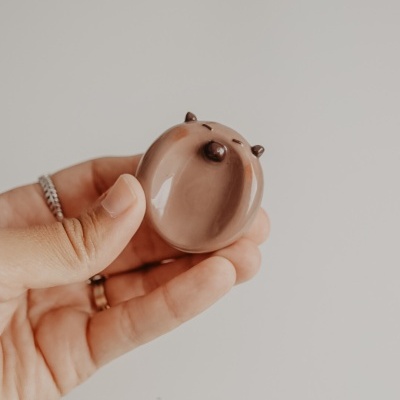 Pequeno objeto cerâmico em forma de animal segurado por mão com fundo neutro