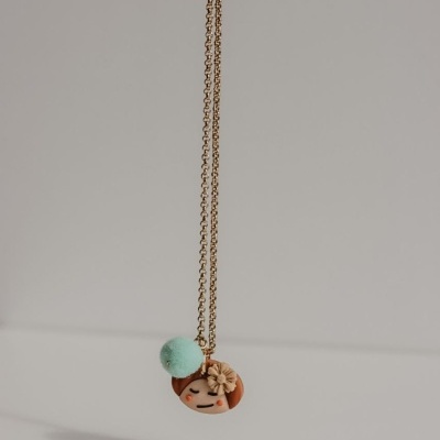 Colar dourado com pendente redondo decorado por rosto sorridente, flor e pompom verde claro
