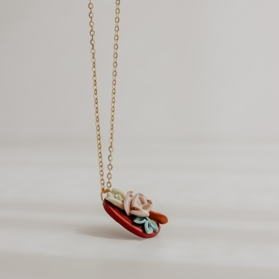 Colar dourado com pendente colorido em formato de taco com flores