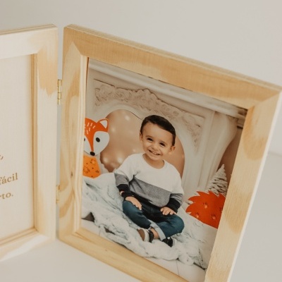 Moldura de madeira clara com fotografia de criança sorridente sentada com peluches laranja