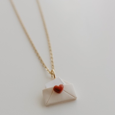 Colar dourado com pendente de envelope e coração vermelho