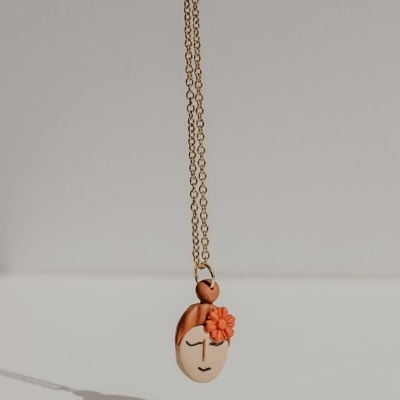 Colar com pendente de rosto estilizado e flor laranja numa corrente dourada