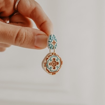 Brinco cerâmico pendente azul, castanho e branco segurado por uma mão