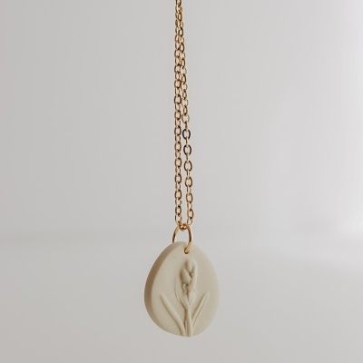 Colar dourado com pendente oval bege e relevo de flor