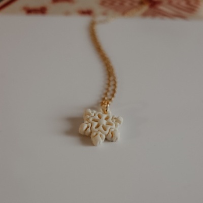 Colar com pendente branco em forma de flor e corrente dourada sobre superfície branca