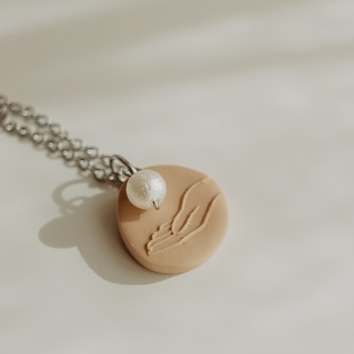 Colar prateado com pendente redondo bege com relevo de mão e esfera perolada