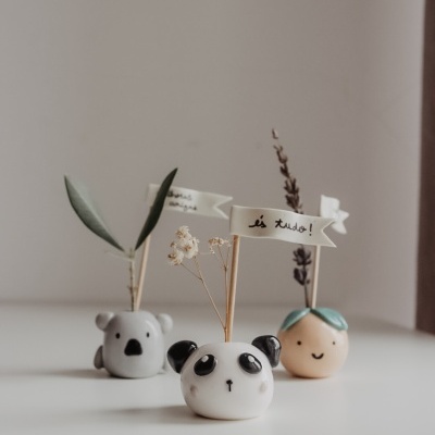 Três mini vasos cerâmicos decorativos com faces de panda, urso e amarelo com folhas, com bandeirinhas em português