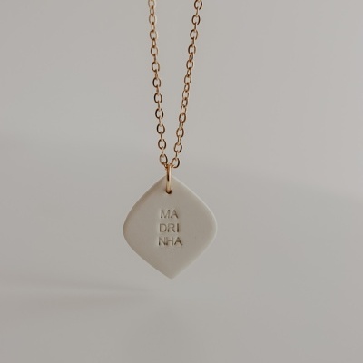 Colar dourado com pendente creme com texto 'MADRINHA'.