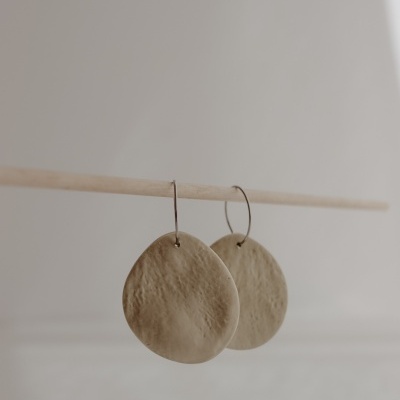 Brincos ovais bege claro com textura pendurados em argolas metálicas finas