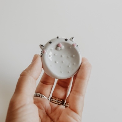 pequeno prato de cerâmica branca com desenho de gato segurado pela mão de uma pessoa