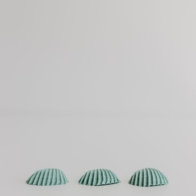 Três objetos verdes semicirculares com textura estriada numa superfície branca