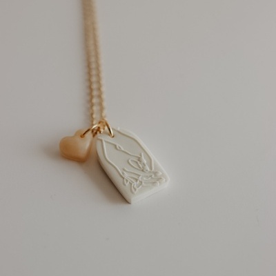Colar com pendentes de coração rosa e placa branca com relevo de mãos em oração