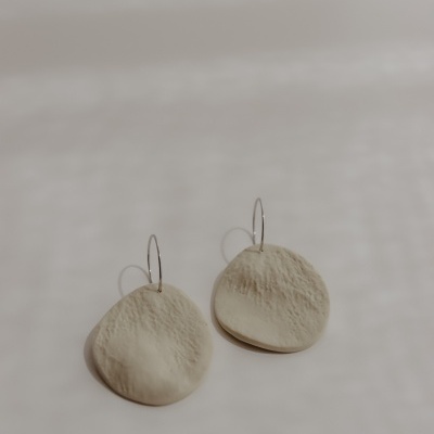 Brincos redondos bege com textura e aro prateado sobre fundo claro