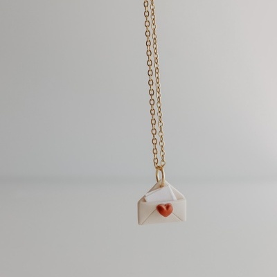 Colar com pendente de envelope branco com selo vermelho em forma de coração.