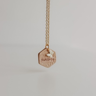 Colar dourado com pendente hexagonal bege com palavra GRIGADO e borboleta branca