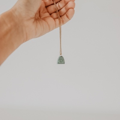 Colar com pendente verde em forma de bolsa segurado por uma mão