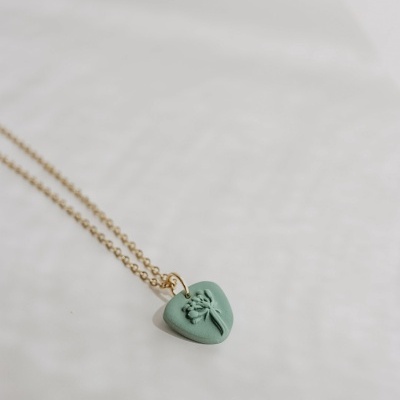 Colar com pendente em forma de coração verde com flor em relevo.
