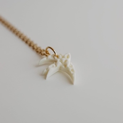 Colar com pendente de pássaro branco e corrente dourada sobre superfície branca