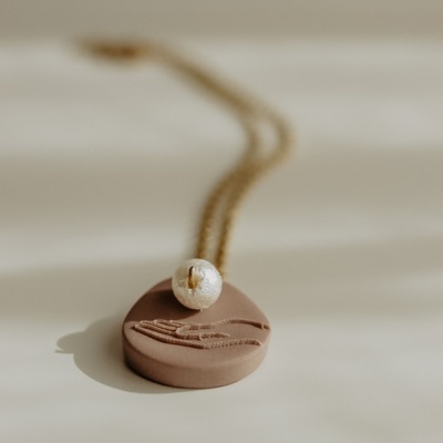 Colar dourado com pendente redondo castanho e pérola branca