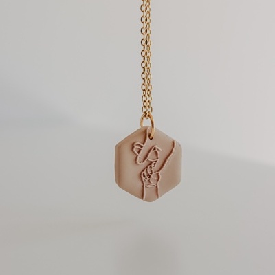Colar com pendente hexagonal bege e relevo de mãos com sinal de paz