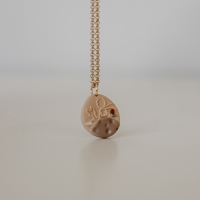 Colar com pendente oval bege e castanho com detalhe floral e corrente dourada