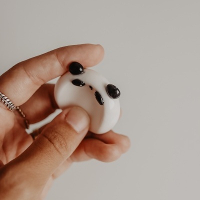 Mão com anel a segurar pequeno objeto branco com detalhes pretos