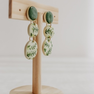 Brincos verdes e brancos com padrão de folhas num suporte de madeira
