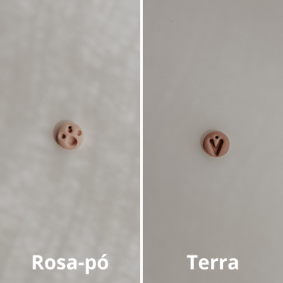 Dois botões redondos, um rosa-pó e outro terra, com diferentes furos e símbolos, sobre fundo claro.
