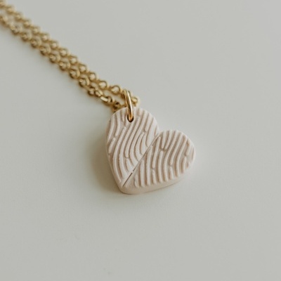Colar dourado com pendente em forma de coração bege com padrão texturizado.