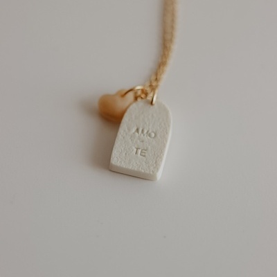 Colar com pendentes coração dourado e retângulo branco com texto 'AMO TE' em fundo branco