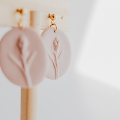 Brincos redondos rosa claro com flores em relevo pendurados numa estrutura de madeira