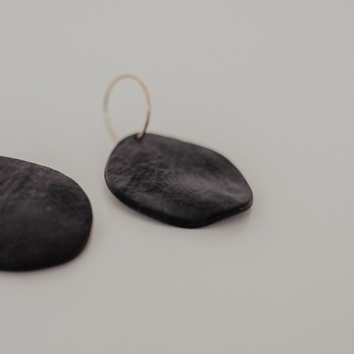 Brincos pretos irregulares com argola dourada numa superfície cinzenta.