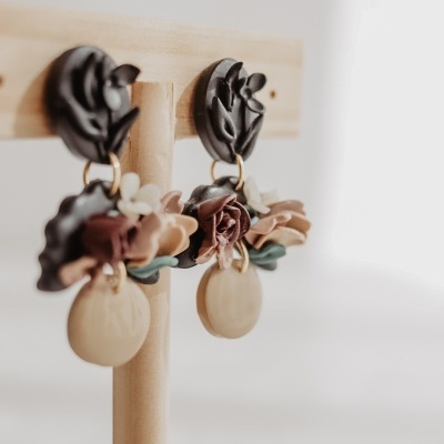 Brincos pendentes com flores e elementos redondos em suporte de madeira