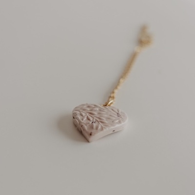 Colar com pendente coração bege texturizado sobre superfície branca