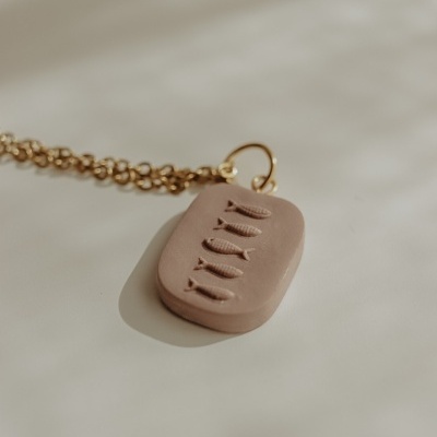 Colar dourado com pendente bege gravado com peixes