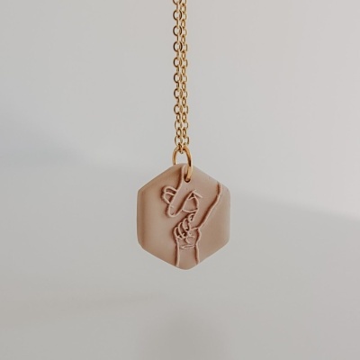 Colar bege com pendente hexagonal e desenho em relevo de mãos entrelaçadas