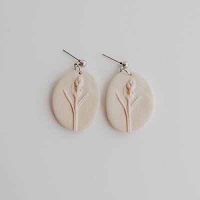 Brincos pendentes ovais creme com relevo floral e pino metálico prateado