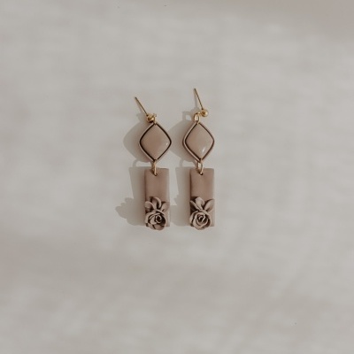 Brincos pendentes em tons neutros com forma losango e flor em relevo