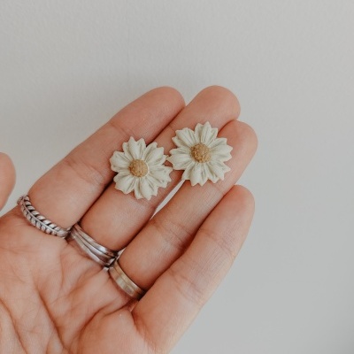 Brincos em forma de margaridas brancas com centro amarelo na mão