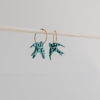 Brincos azul-turquesa texturizados em argolas douradas pendurados num pau fino