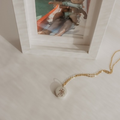 Colar dourado com pendente branco com desenho junto a moldura branca com fotografia de crianças