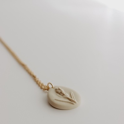 Colar dourado com pendente redondo bege com relevo de flor