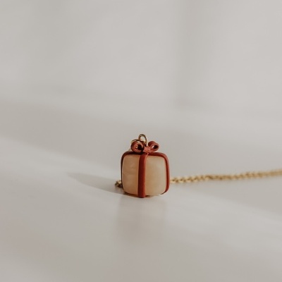 Colar com pendente de presente branco com fita vermelha sobre superfície branca