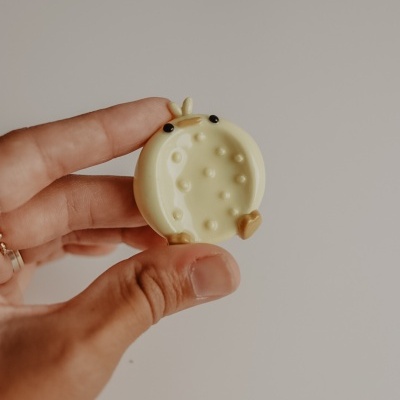 Objeto redondo amarelo claro com textura de bolinhas na mão, fundo branco