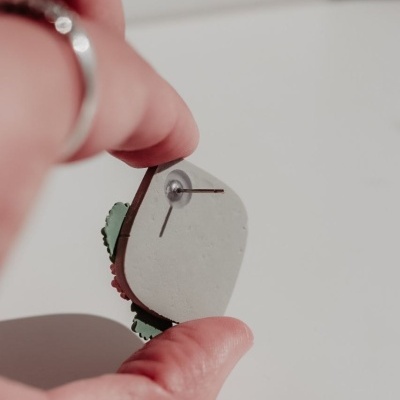 Brinco com base branca e borda colorida segurado por mão com anel