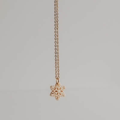 Colar dourado com pendente de flor creme suspenso contra fundo cinzento