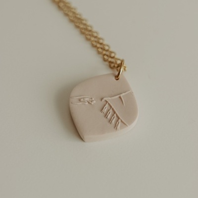 Colar dourado com pendente bege claro com relevo de mãos e tecido
